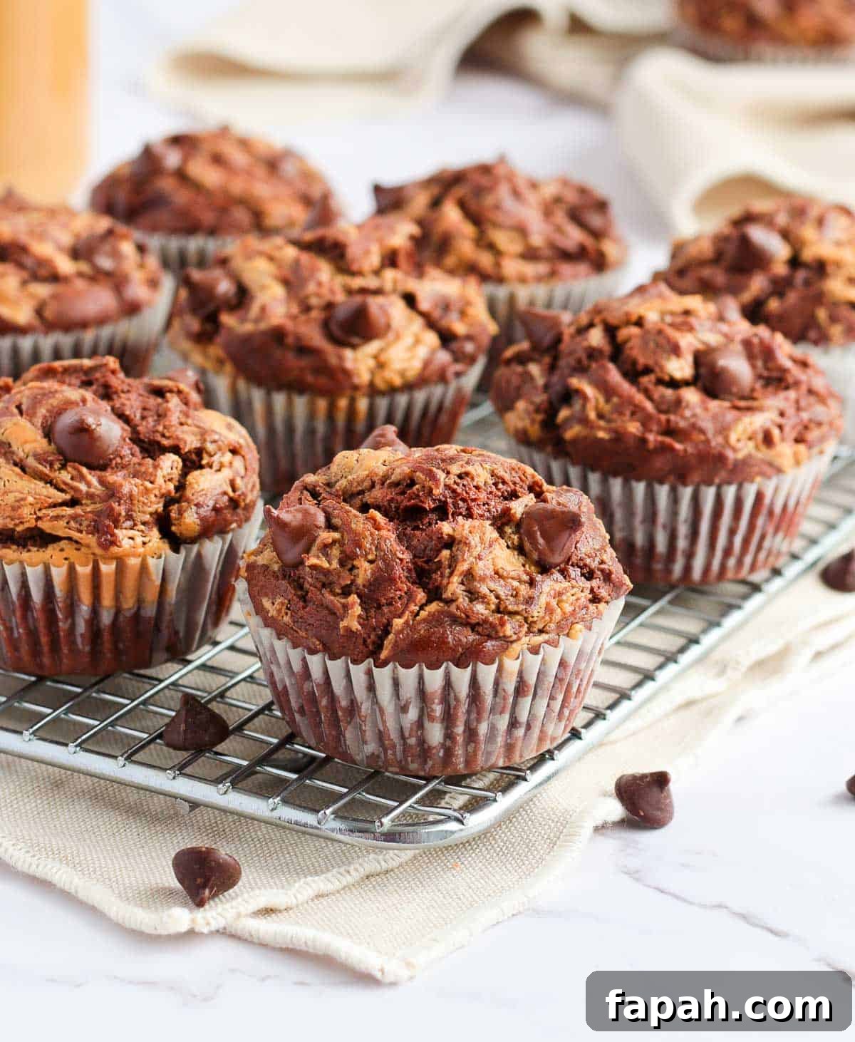 Muffins on a cooling rack over a beige tea towel.