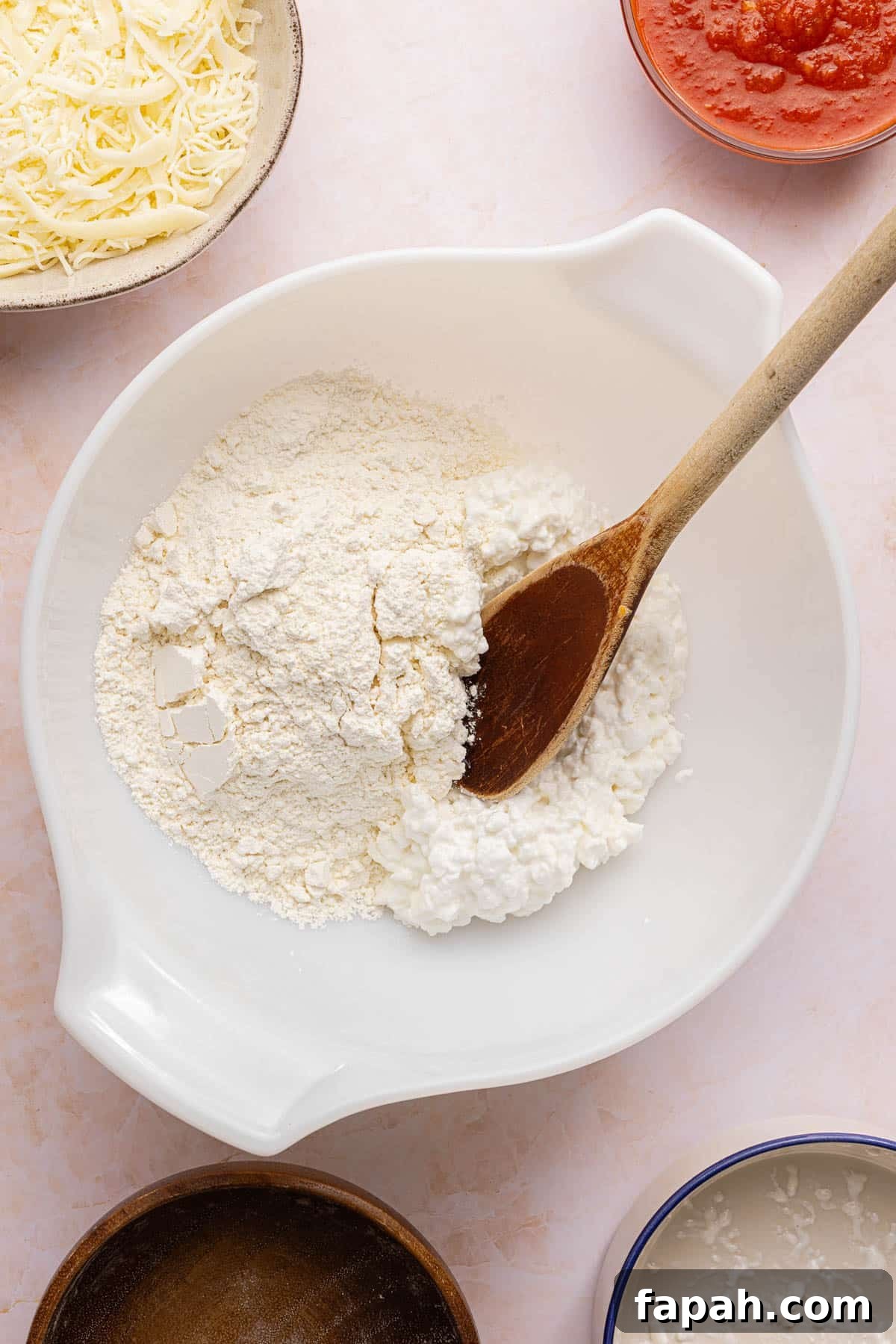 The self-rising flour and cottage cheese in a white bowl on a countertop with a wooden spoon in it.