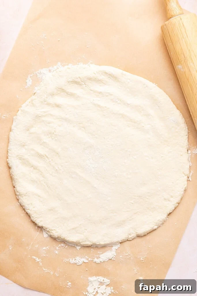 The pizza dough rolled into a round circle on the piece of parchment paper.