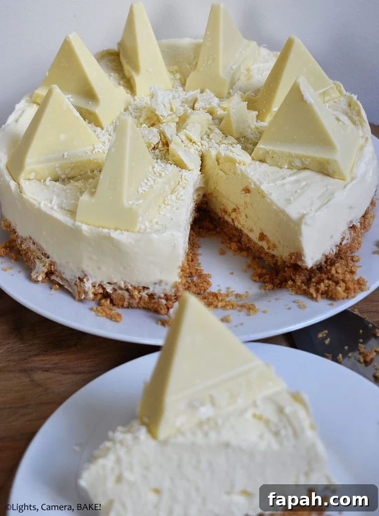 Vertical view of a slice of White Chocolate Toblerone Cheesecake on a white plate with the full cheesecake in the background.