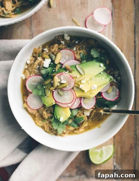 A white bowl filled with pozole verde, topped with sliced radishes, pepitas, avocado, and cilantro.