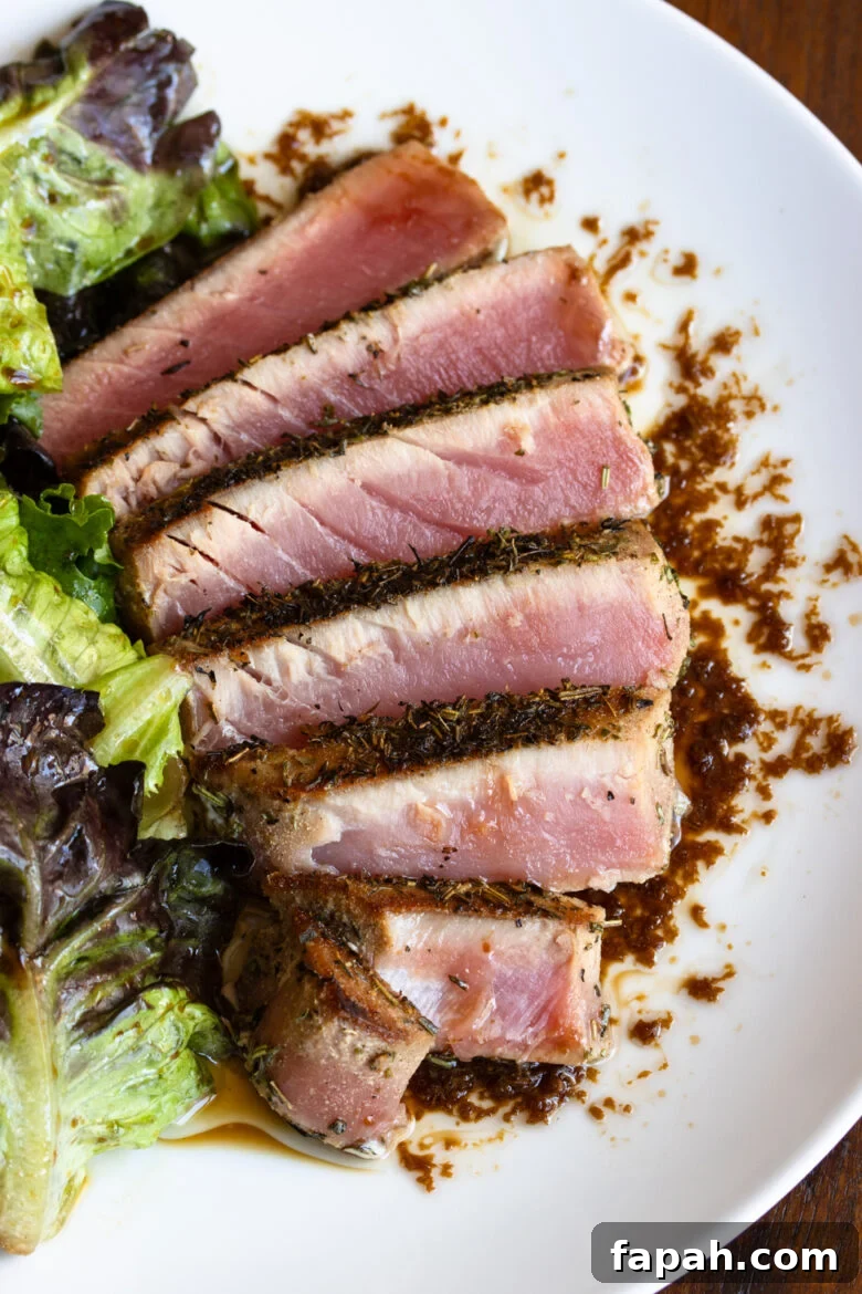 Grilled tuna steak sliced and fanned out on a white plate with salad alongside.