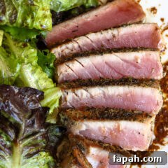Grilled tuna steak fanned out on a white plate with the dressing and salad alongside.