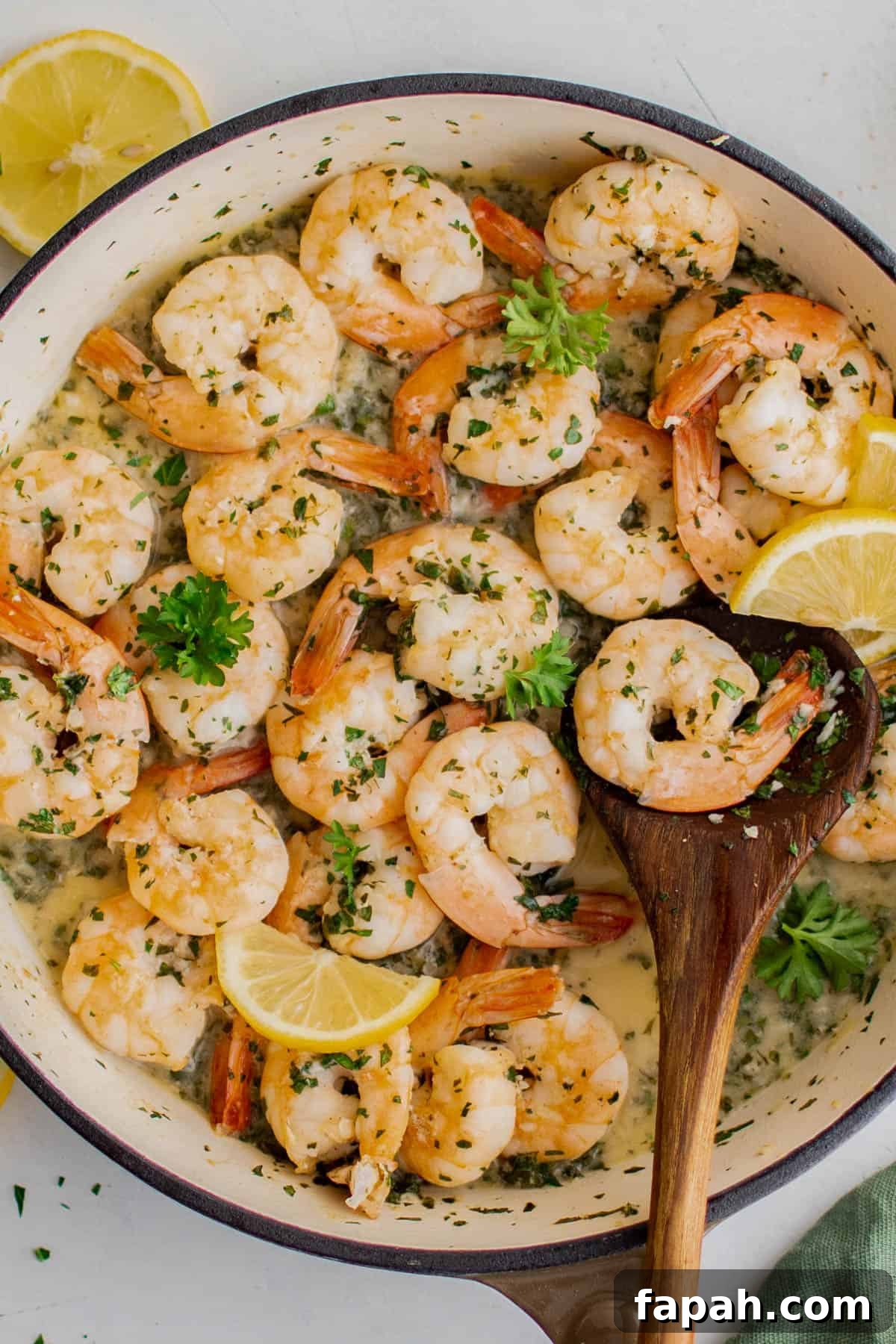 Garlic Lemon Shrimp Recipe with Zesty Butter Sauce 2 A skillet with cooked lemon garlic shrimp and a wooden spoon lifting the shrimp out of the pan.