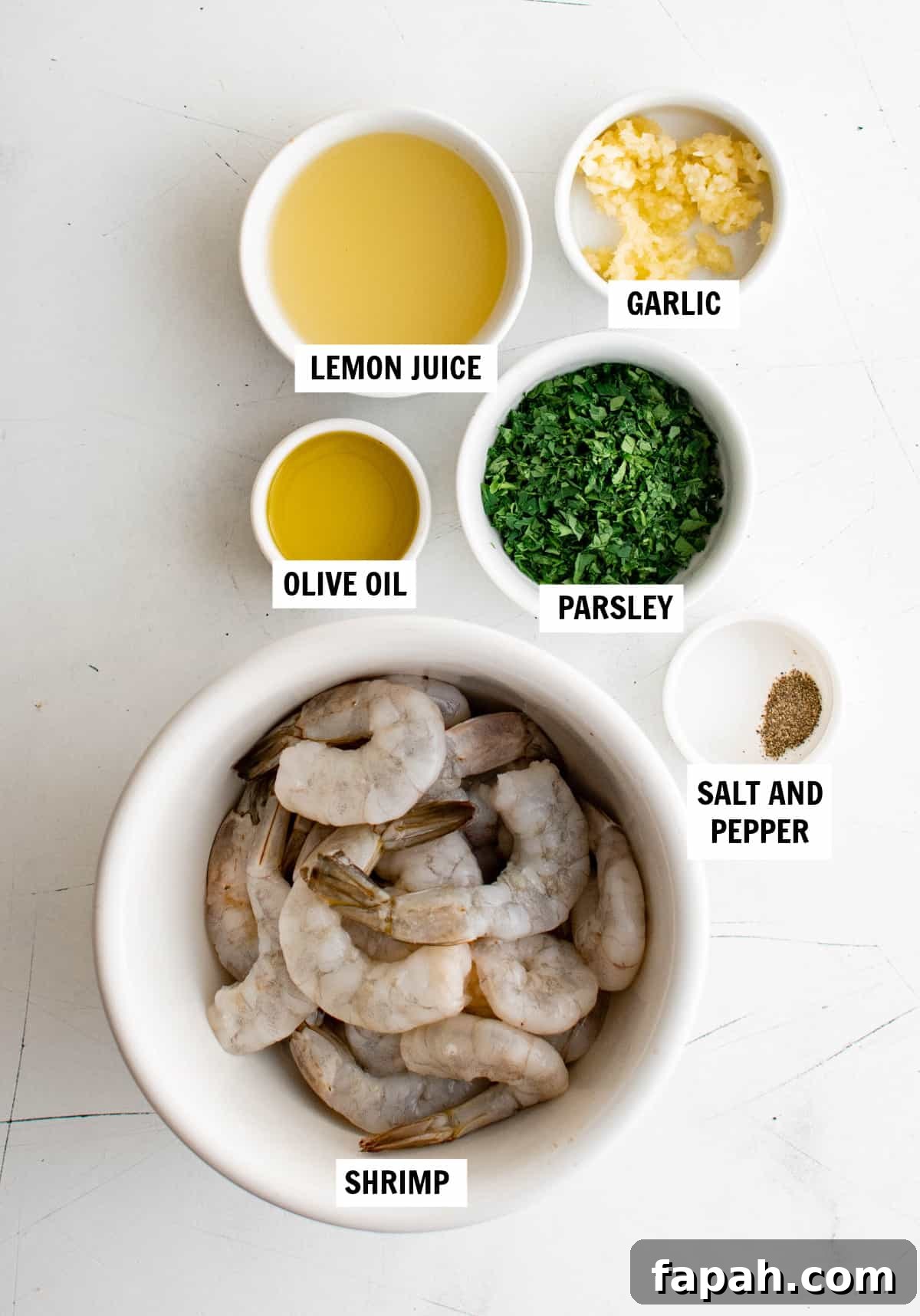 Garlic Lemon Shrimp Recipe with Zesty Butter Sauce 3 All of the ingredients for lemon garlic shrimp on a white countertop including peeled and deveined shrimp, olive oil, lemon juice, garlic, parsley, salt and pepper.