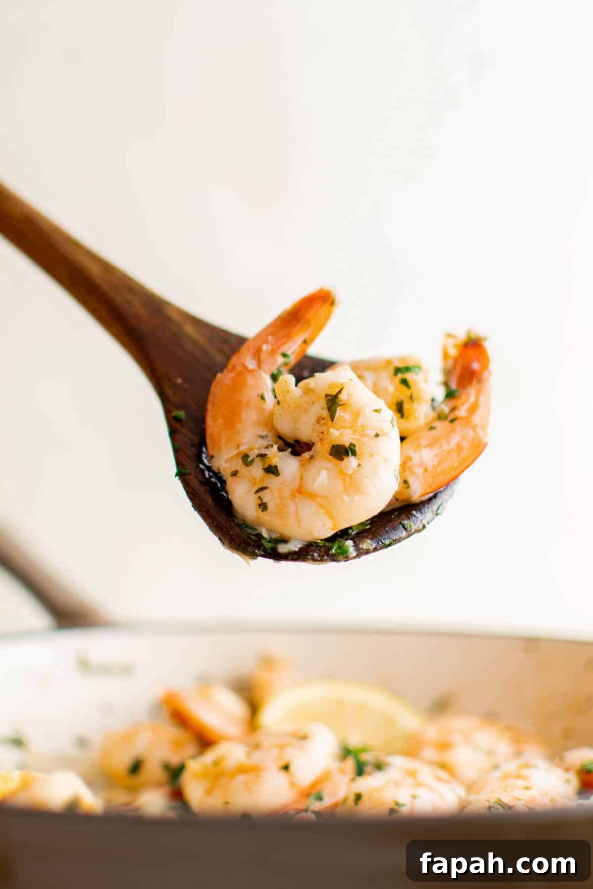 Garlic Lemon Shrimp Recipe with Zesty Butter Sauce 6 A wooden spoon serving two pieces of lemon garlic shrimp from the pan.