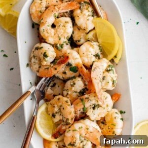 Garlic Lemon Shrimp Recipe with Zesty Butter Sauce 7 Cooked lemon garlic shrimp on a white serving plate with serving fork and lemon wedges.