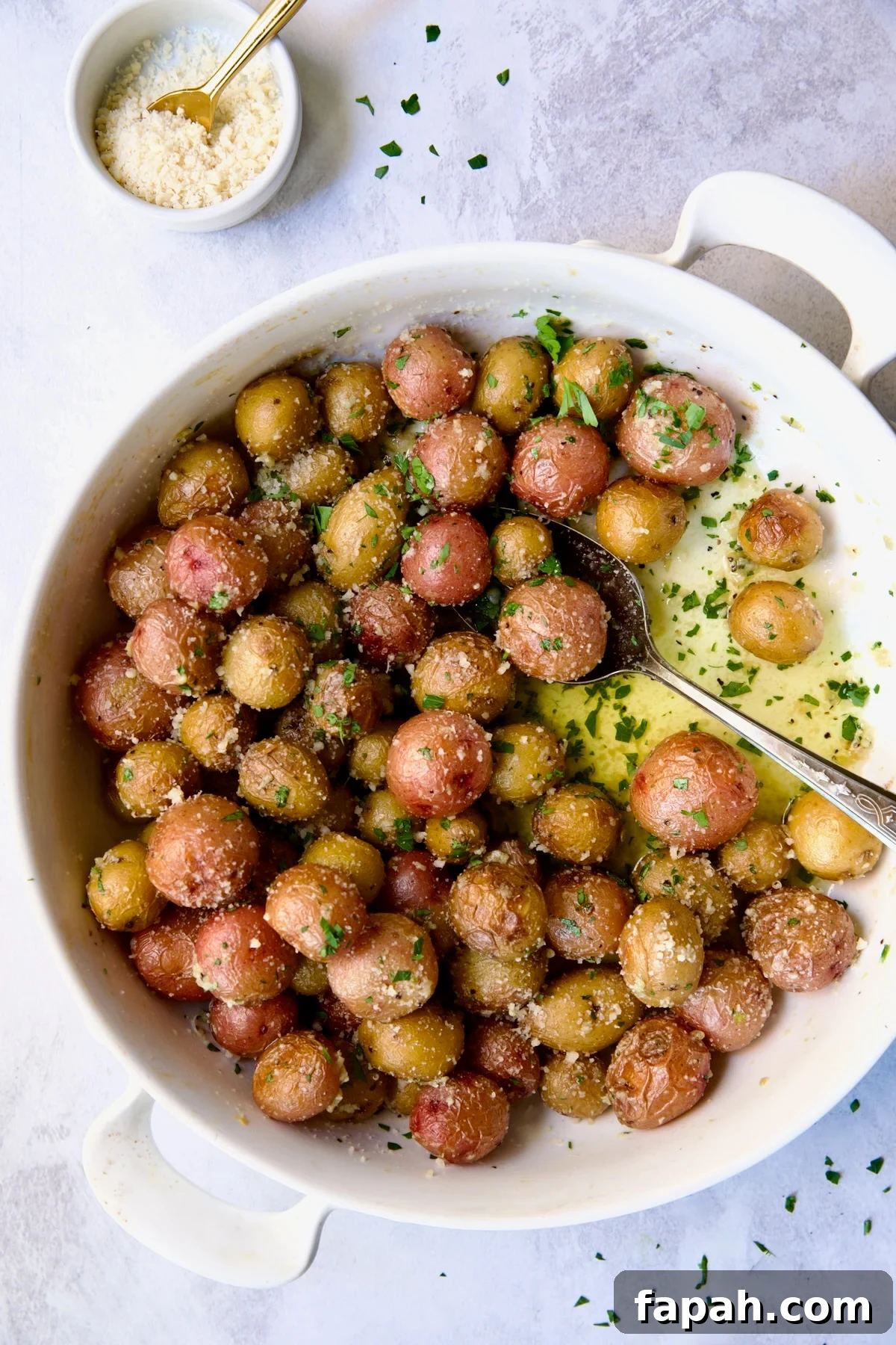 Garlic Butter Parmesan Mini Potatoes in round white baking dish with serving spoon.