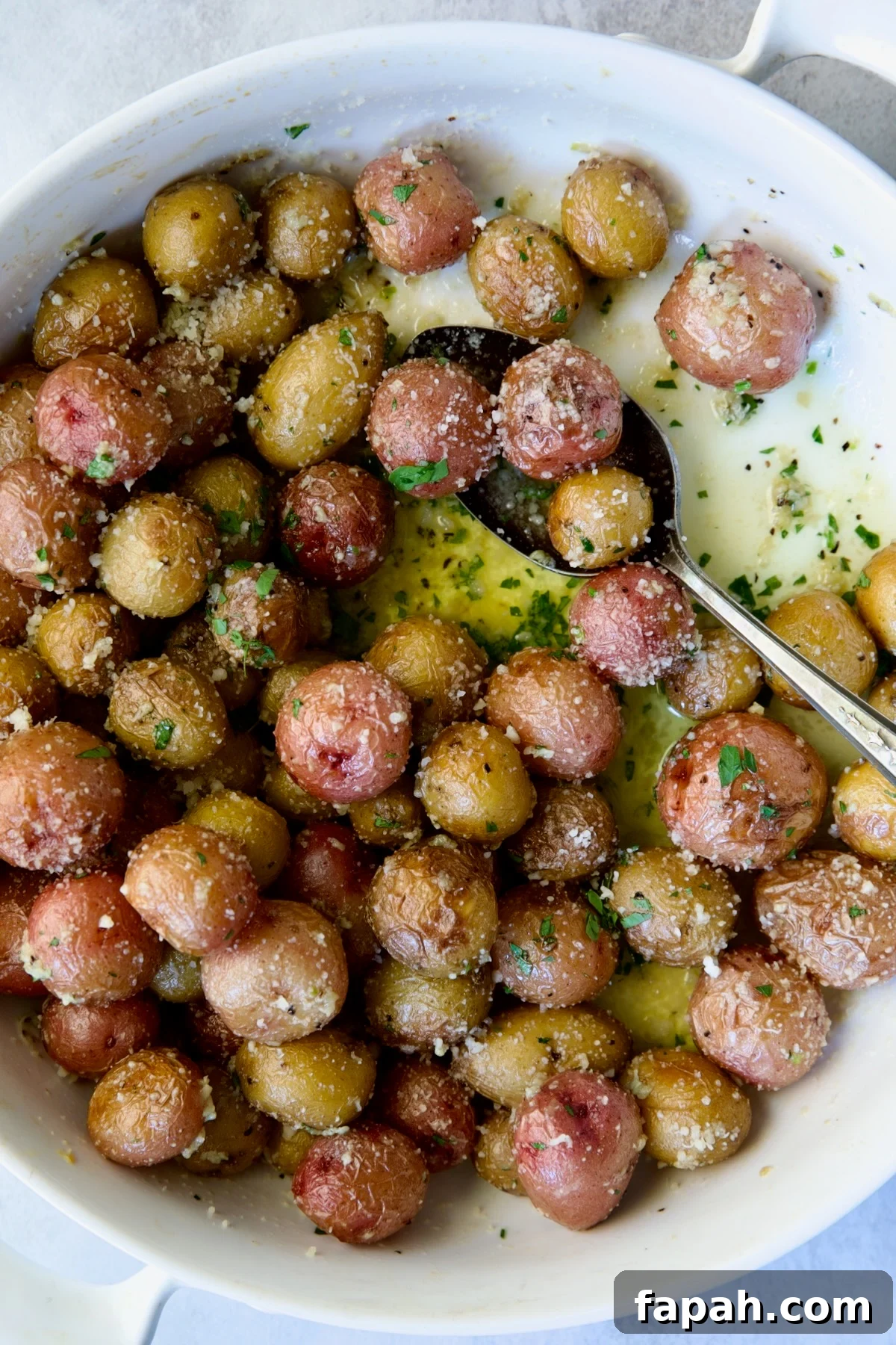 Garlic Butter Parmesan Mini Potatoes in round white baking dish with serving spoon.