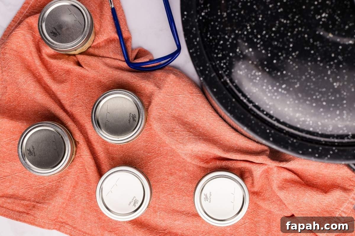 Sealed mustard jars cooling on orange towel next to canning pot.