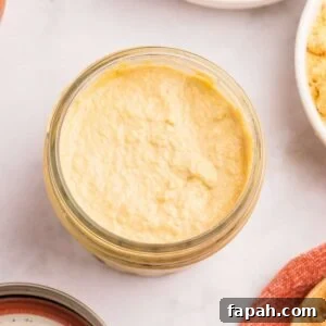 Jar of homemade yellow Dijon mustard with mustard seeds in bowls nearby.