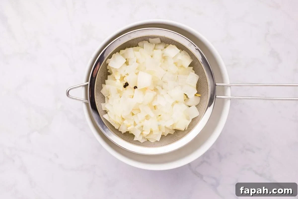 Fine mesh strainer with cooked onion mixture being strained into bowl.