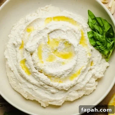 Vegan Ricotta cheese in a white bowl with olive oil drizzled on top and basil leaves on the side.