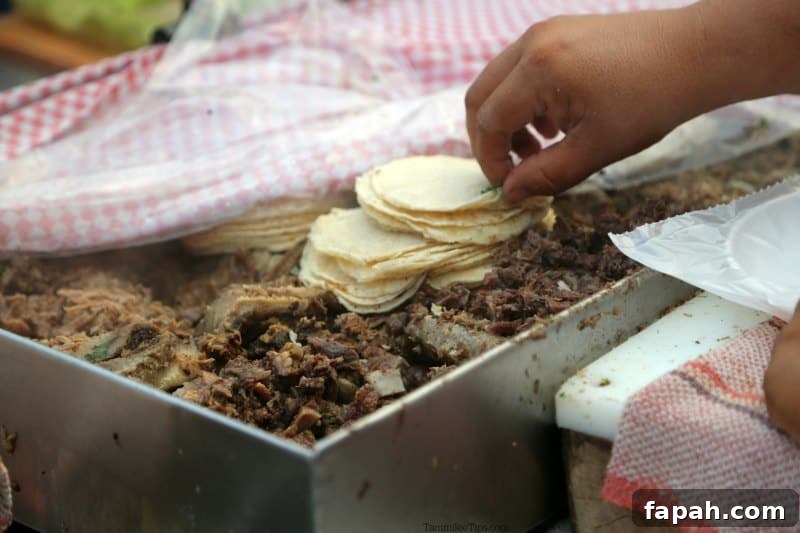 hand reaching for tortillas over a grill filled with meat 