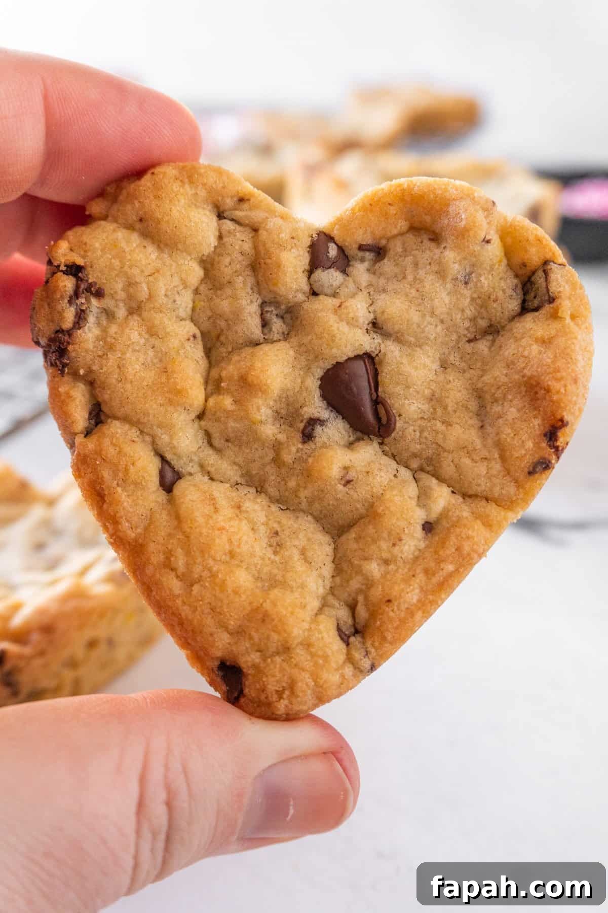 Heart-Shaped Cookies Recipe for Valentine’s Day 14 holding heart shaped chocolate chip cookie.