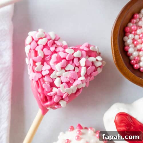 Pink heart-shaped cake pop covered in heart sprinkles.