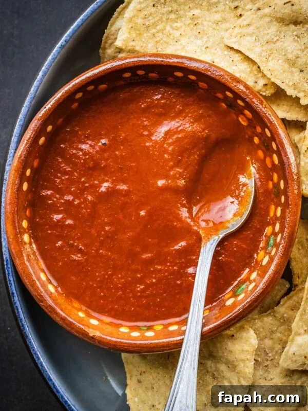 Fresh Cherry Tomato Pico de Gallo Salsa Recipe 10 Salsa roja in a terracotta bowl with a spoon on a plate with some tortilla chips.
