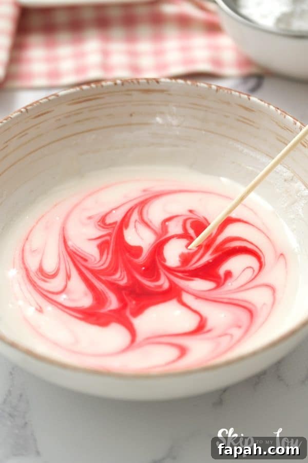 White ceramic mixing bowl with confectioner's icing and red icing gel swirled around with a wooden mixing stick, by Skip to my Lou.