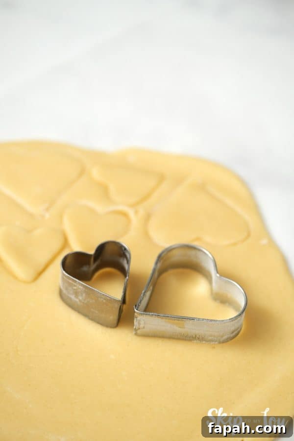Two heart-shaped cookie cutters sitting on top of a slab of rolled out cookie dough, by Skip to my Lou.