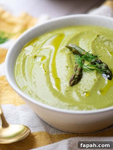 Close up of asparagus leek soup in a white bowl over a yellow striped linen.