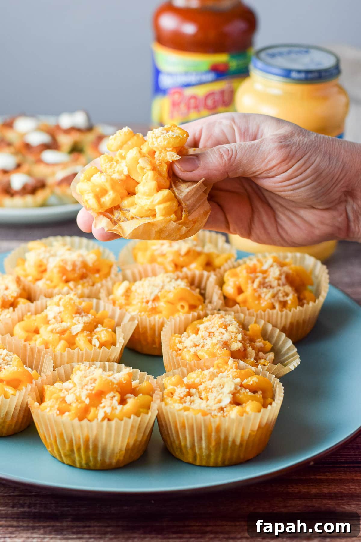 A hand holding the mac and cheese appetizer held over the plate