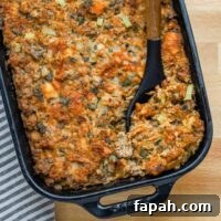 Savory Sausage and Brioche Stuffing Recipe 2 Sausage brioche dressing in a baking dish with a large spoon.