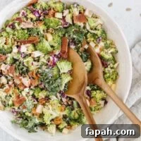 Broccoli salad with kale and red cabbage in a large serving bowl with wooden salad utensils in the bowl.