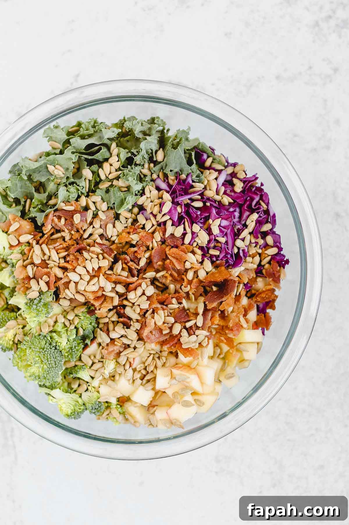 broccoli, kale, bacon, cabbage, apples, sunflower seeds in a glass mixing bowl