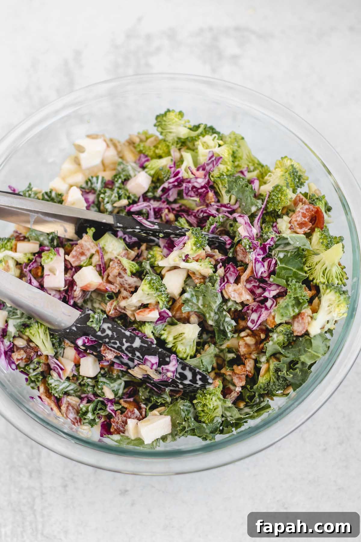 tongs mixing together broccoli salad and dressing