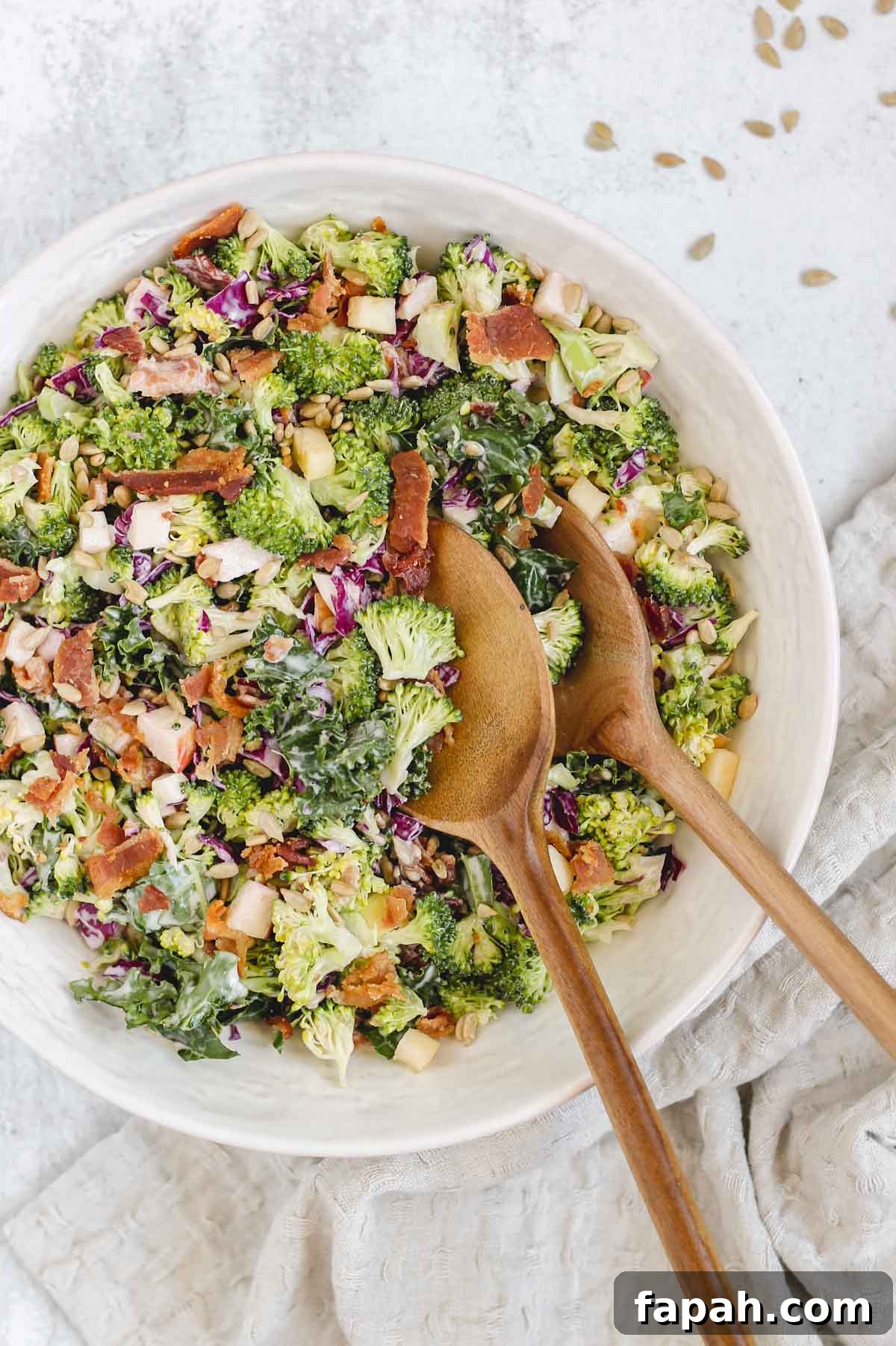broccoli kale salad in white bowl with wooden salad utensils