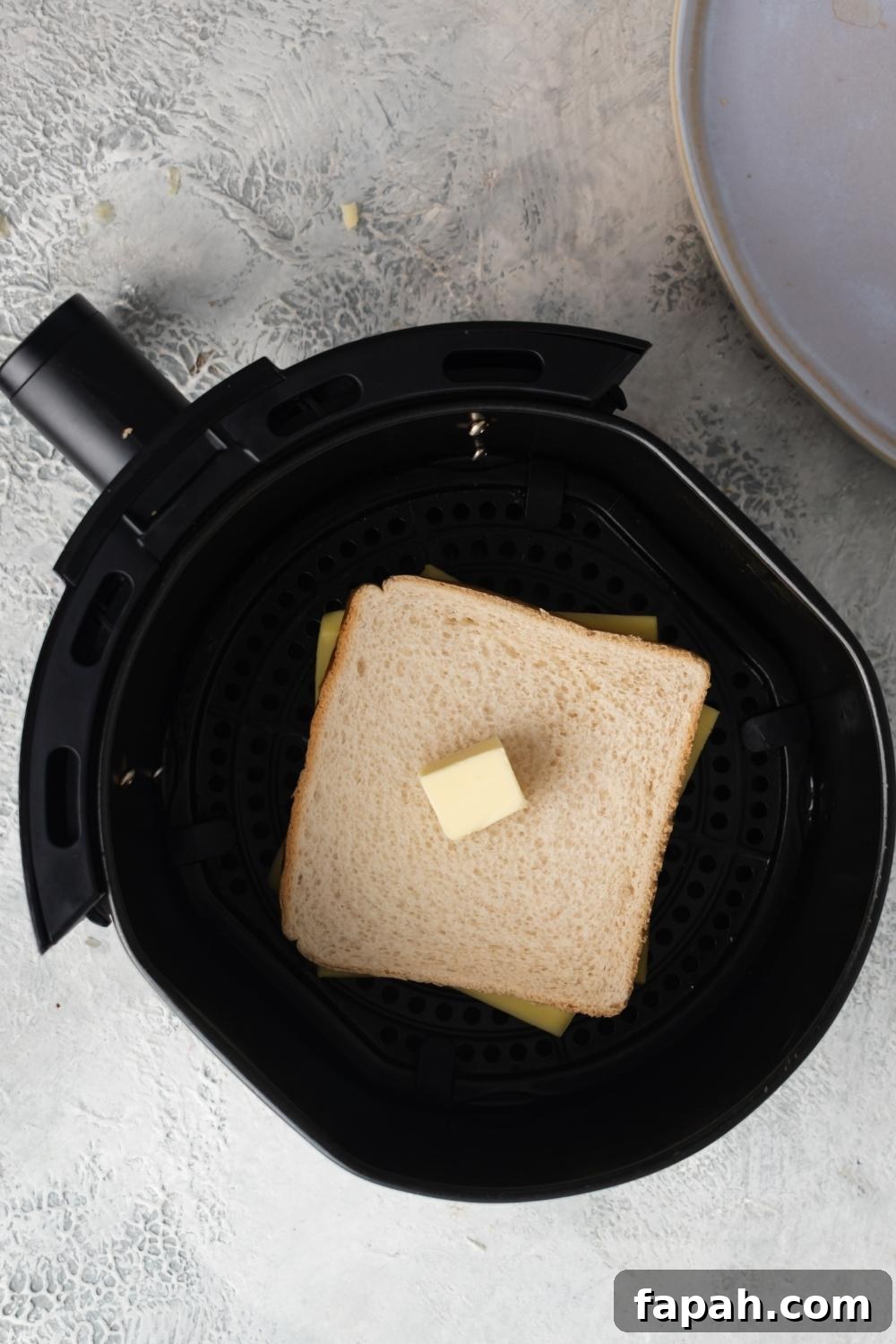 An overhead view of an air fryer with white bread buttered with cheese in the middle.