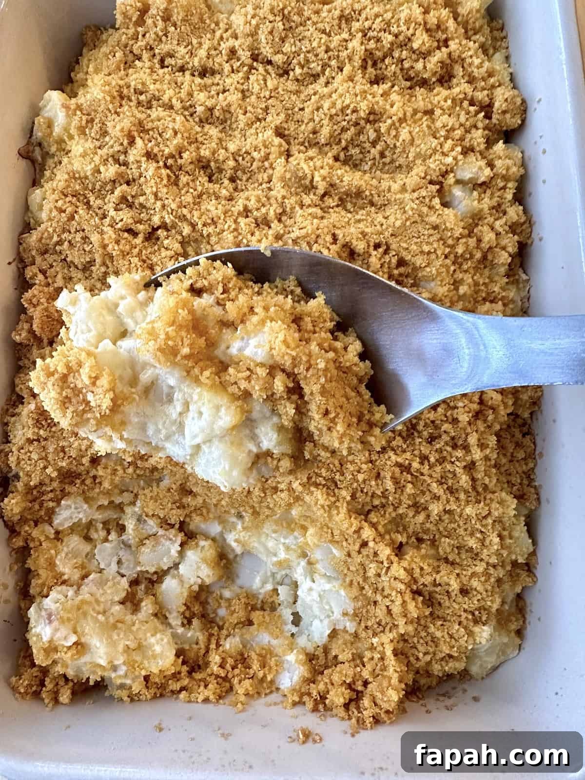 A serving spoon scooping up a serving of potato casserole from a baking dish.
