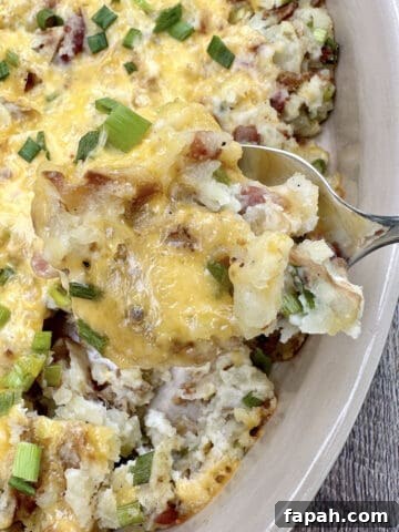 A large spoon scooping up a serving of twice baked potatoes from a baking dish.