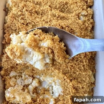 A serving spoon scooping up a serving of potato casserole from a baking dish.