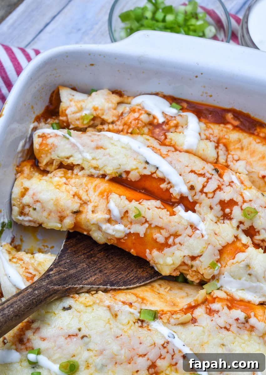 a wooden spatula scooping buffalo chicken enchiladas out of a white baking dish