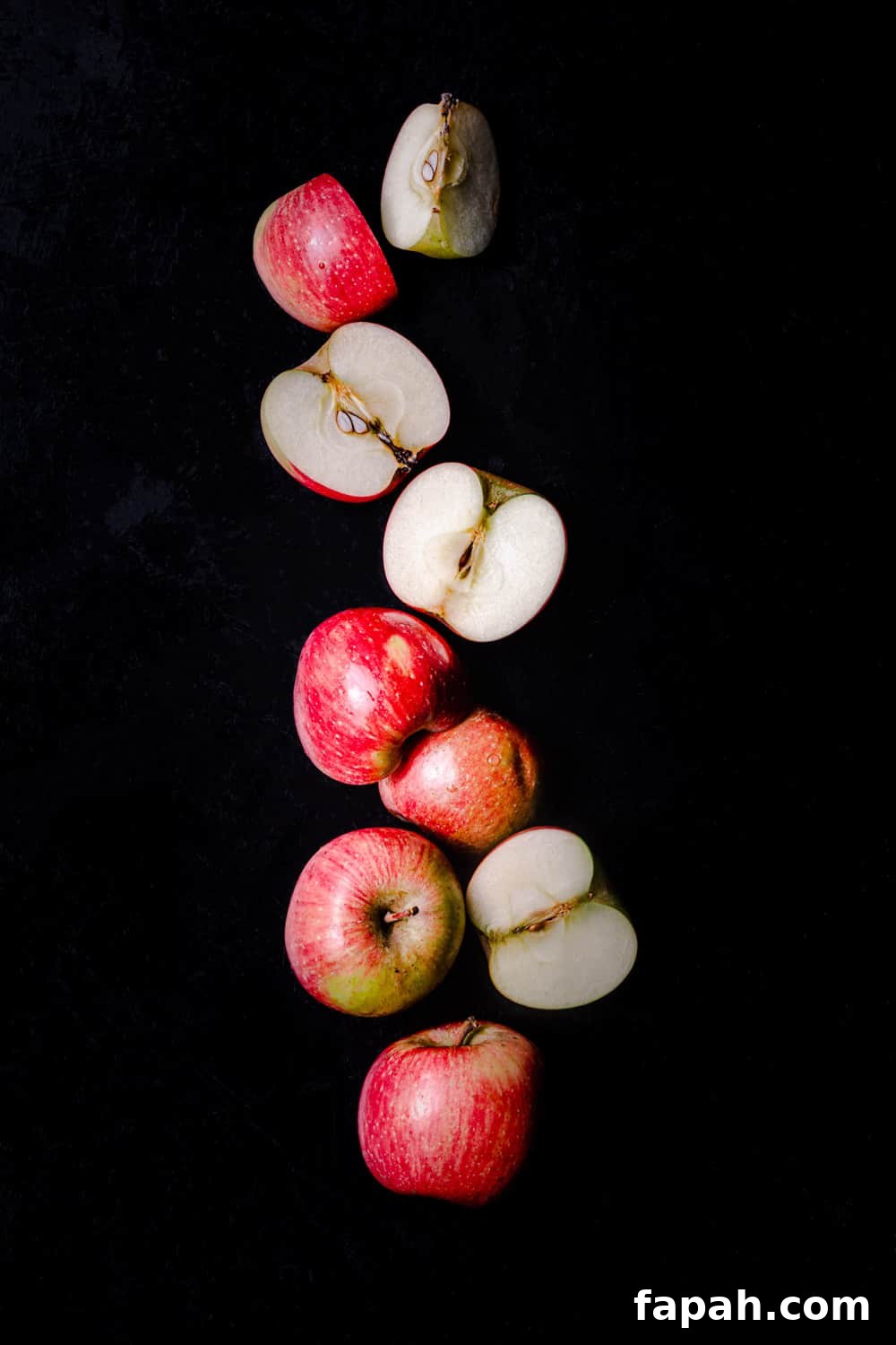 Little red apples, whole, cut in half and quartered, on a black background; overhead shot.