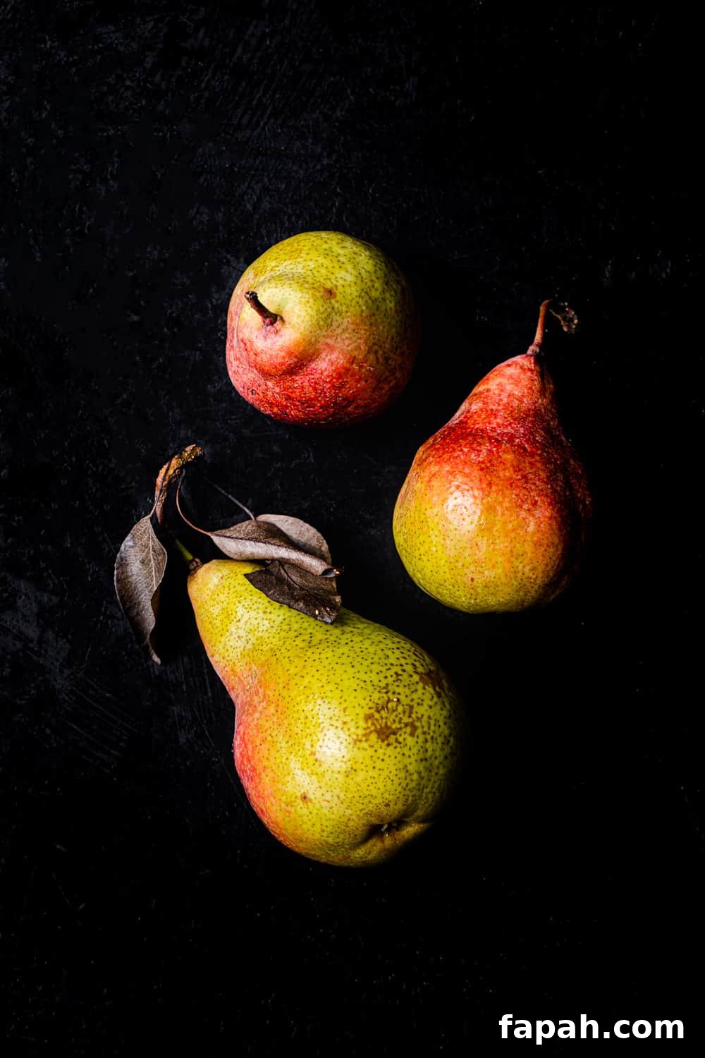3 green and red pears shot lying down and standing up on a black background; overhead shot.
