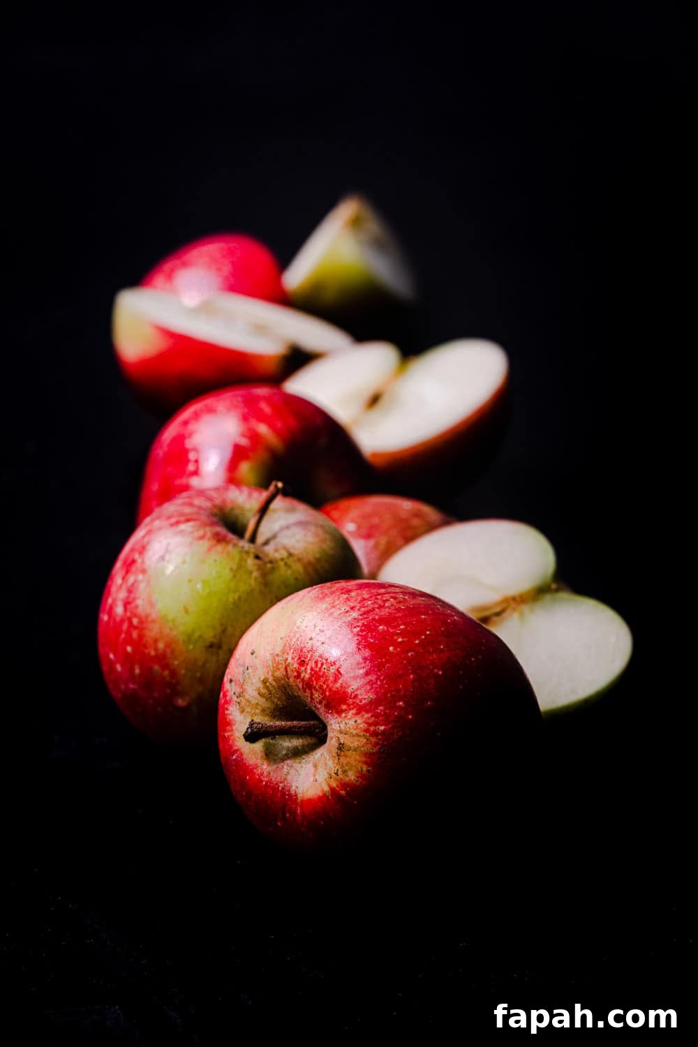 Little red apples, side angle shot, whole, cut in half and quartered; on a black background.