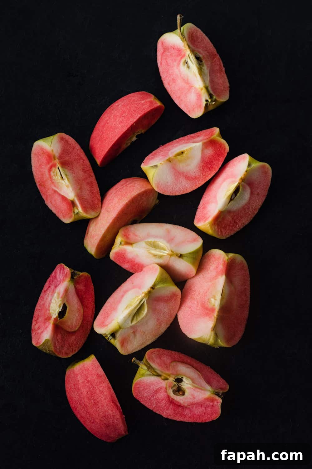 Pink Hidden Rose apples, cut into quarters, on a black background; overhead shot.