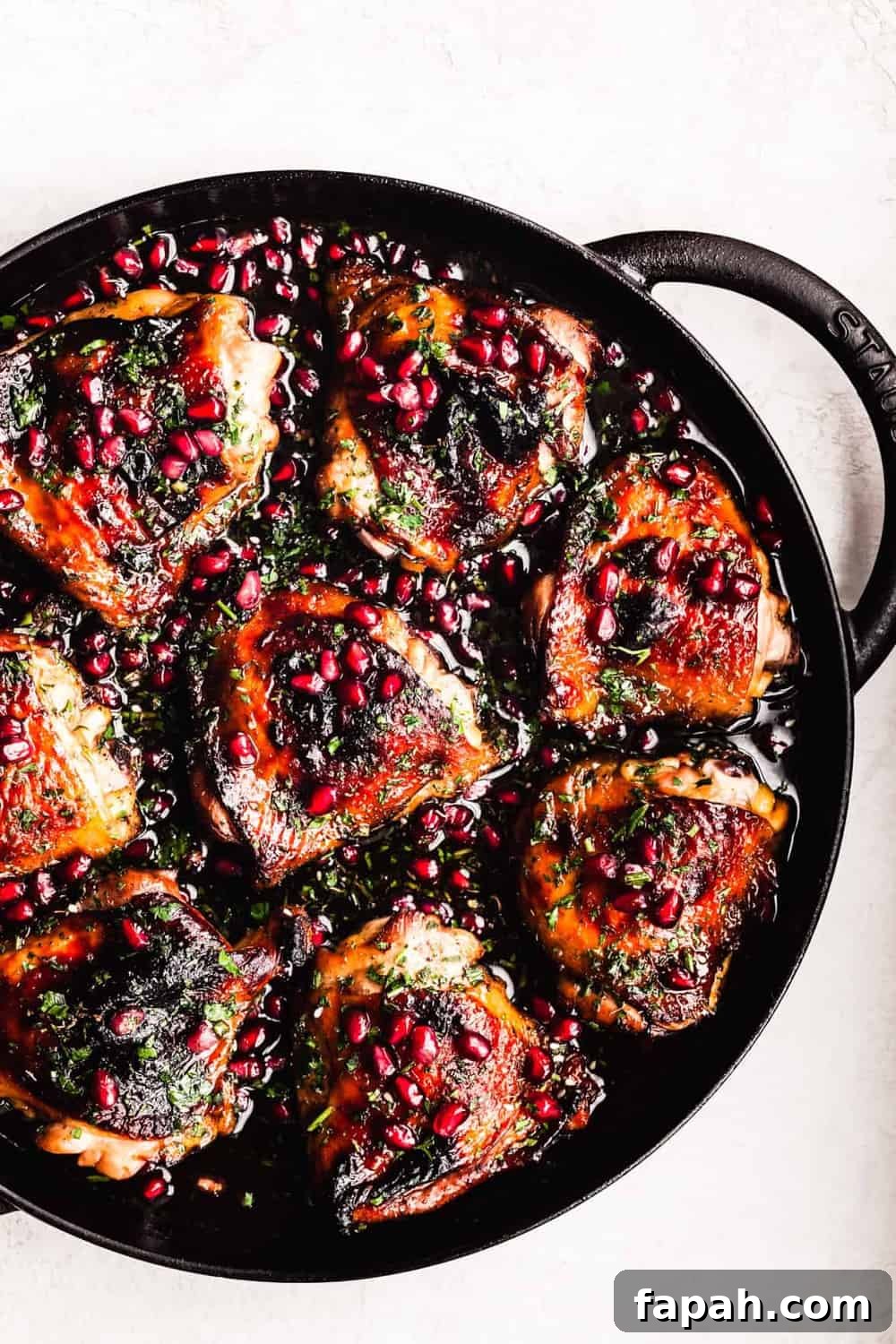 Pomegranate chicken topped with arils and parsley in a cast iron skillet.