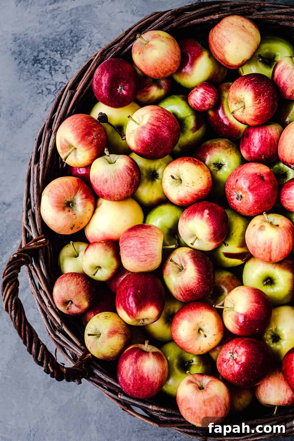 Little apples in a woven basket, with the right side cut off and on a grey background; overhead shot.