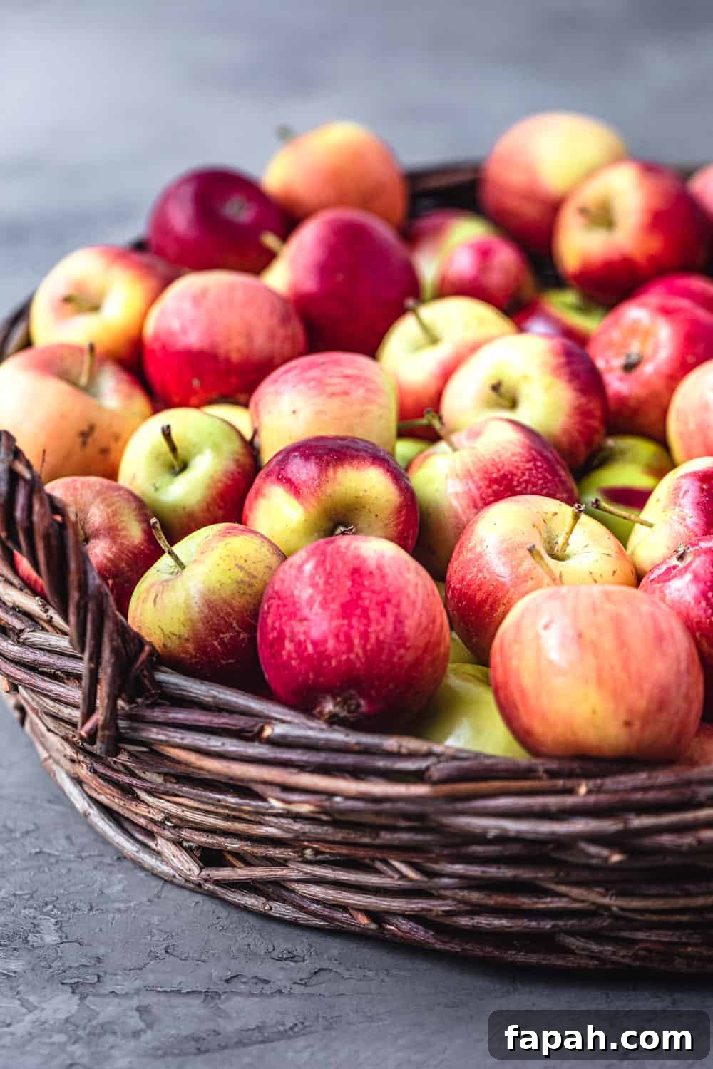 Little apples in a woven basket with handles; side angle shot on a grey background.