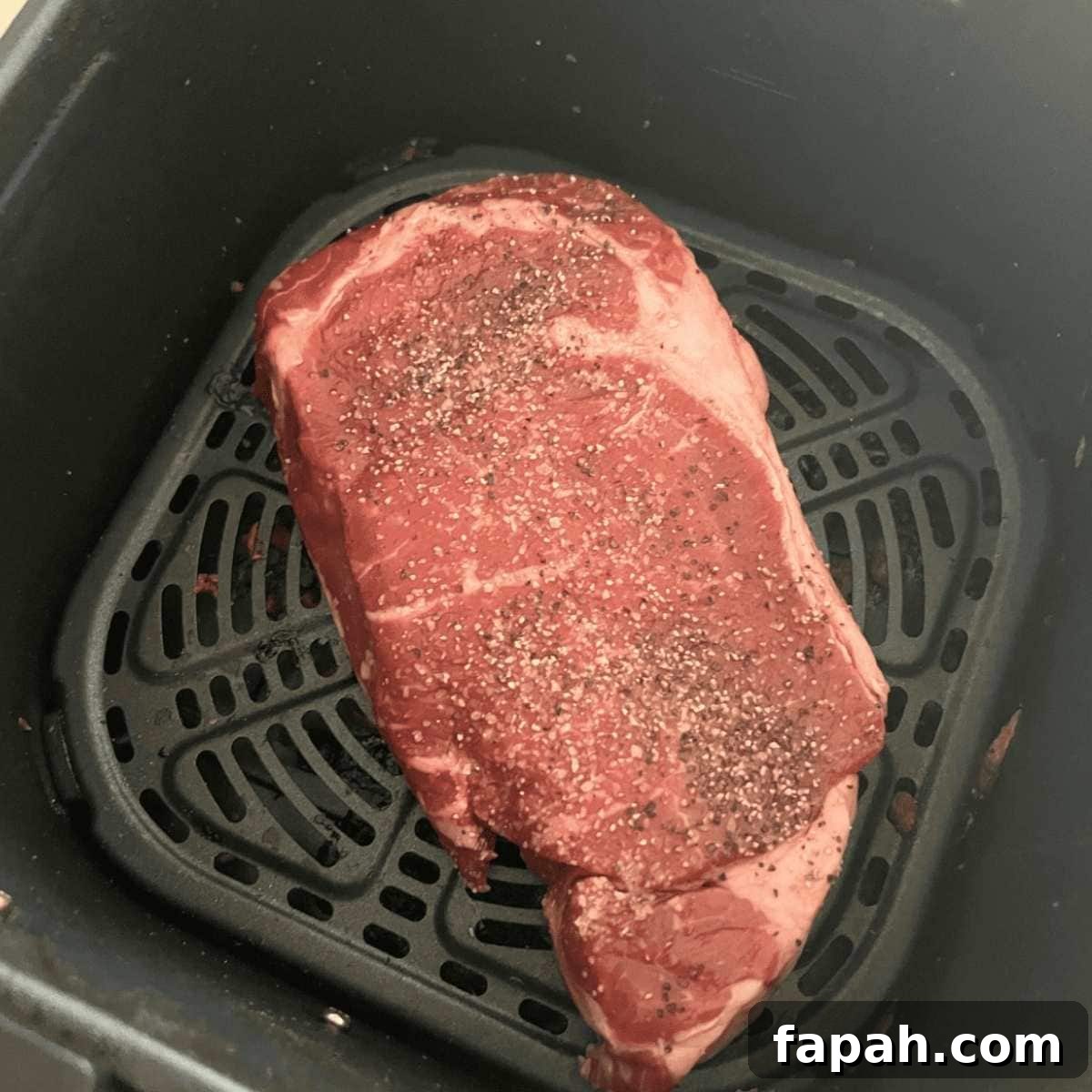 Seasoned steak in air fryer basket. 