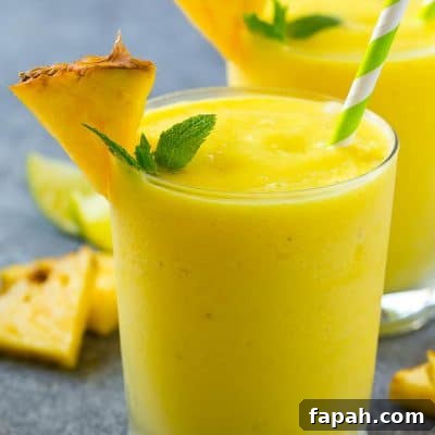 A glass of pineapple smoothie garnished with fresh pineapple and mint.