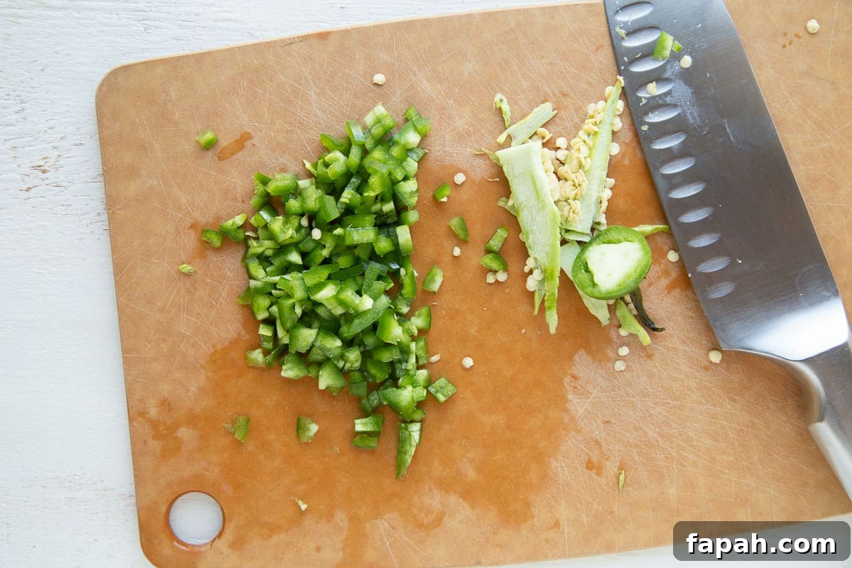 chopped jalapeño on a wooden cutting board next to a knife.