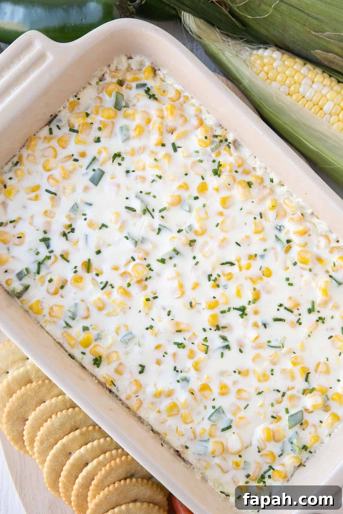 casserole dish filled with cream cheese corn dip next to a row of crackers.