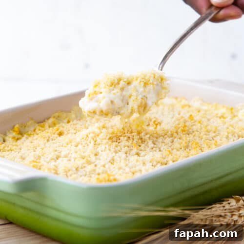 hand lifting a spoon of cheesy corn casserole out of a casserole dish.