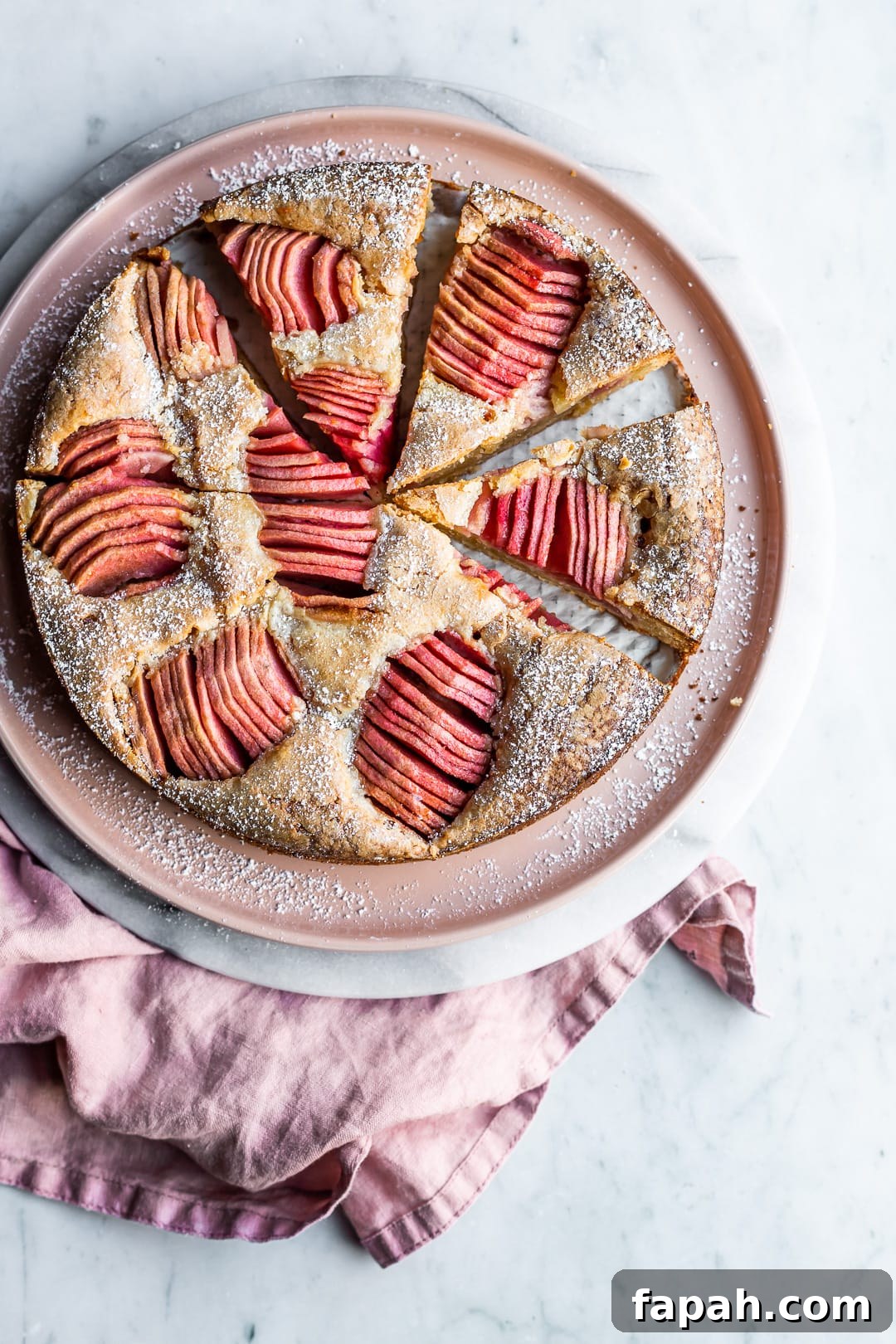 Almond Cake with Roasted Pink Apples 2 Sliced almond cake with pink apples on pink plate and marble surface