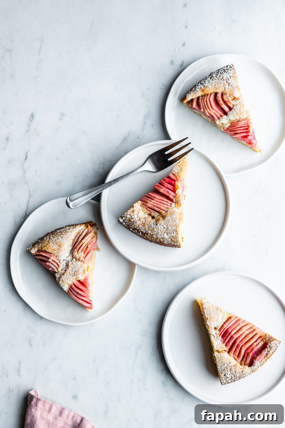 Almond Cake with Roasted Pink Apples 4 Slices of almond cake with pink apples on four white plates on a marble background