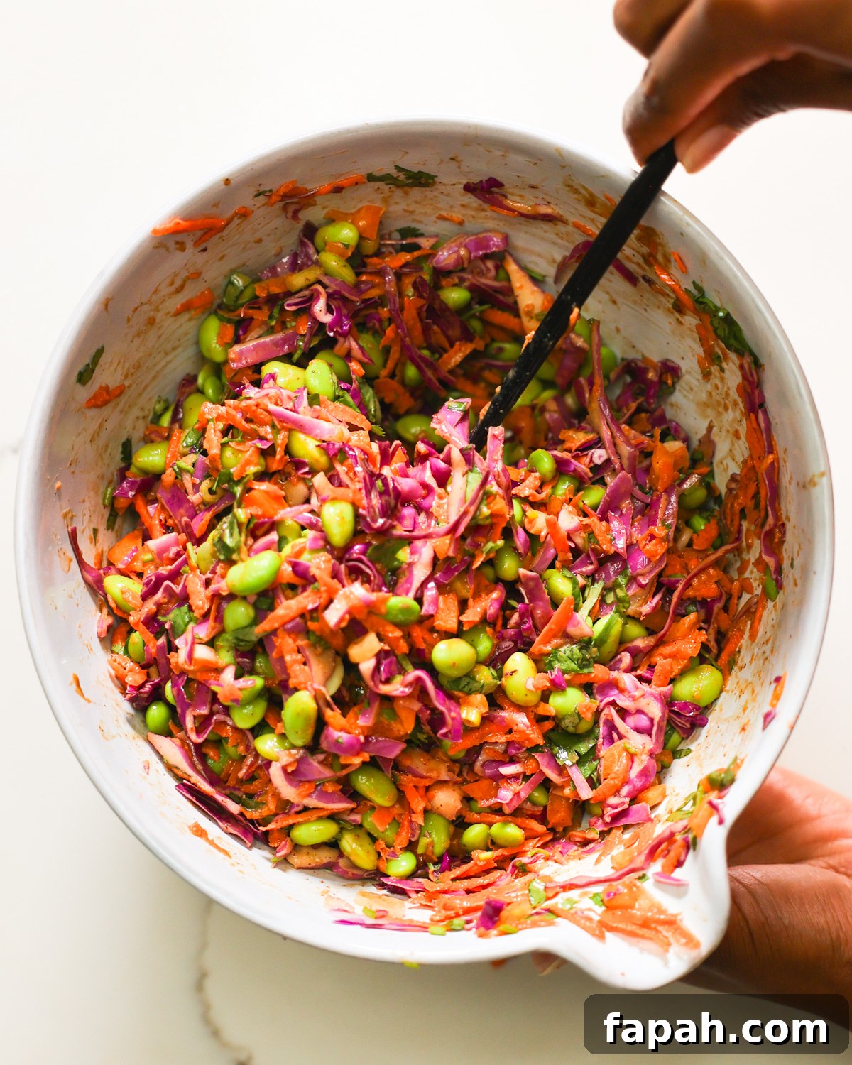 Crisp Edamame Salad with Lemon-Ginger Vinaigrette 8 A brown hand stirring a bowl of edamame salad.